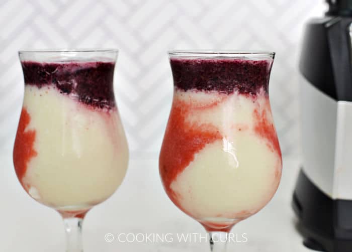 Strawberry, white pina colada, and blueberry layers in shaped glasses. 