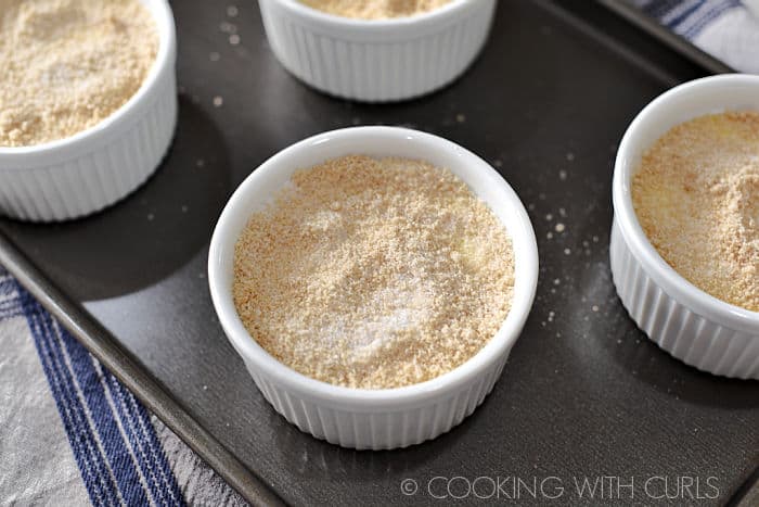 Sugar mixture sprinkled over the top of four creme brulee in white ramekins. 
