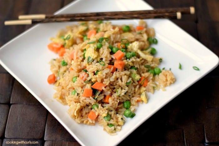 A serving of fried rice on a square white plate with two wooden chopsticks laying across the top corner of the plate