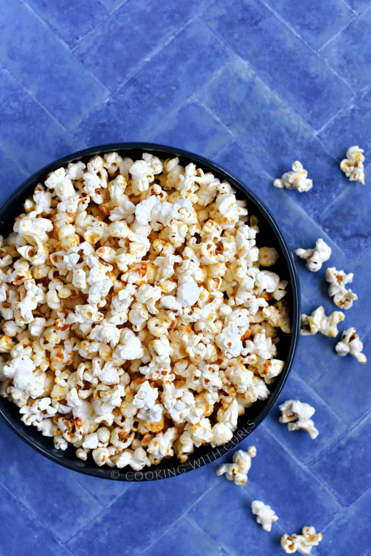 A bowl full of kettle corn popcorn sitting on a blue tile background.