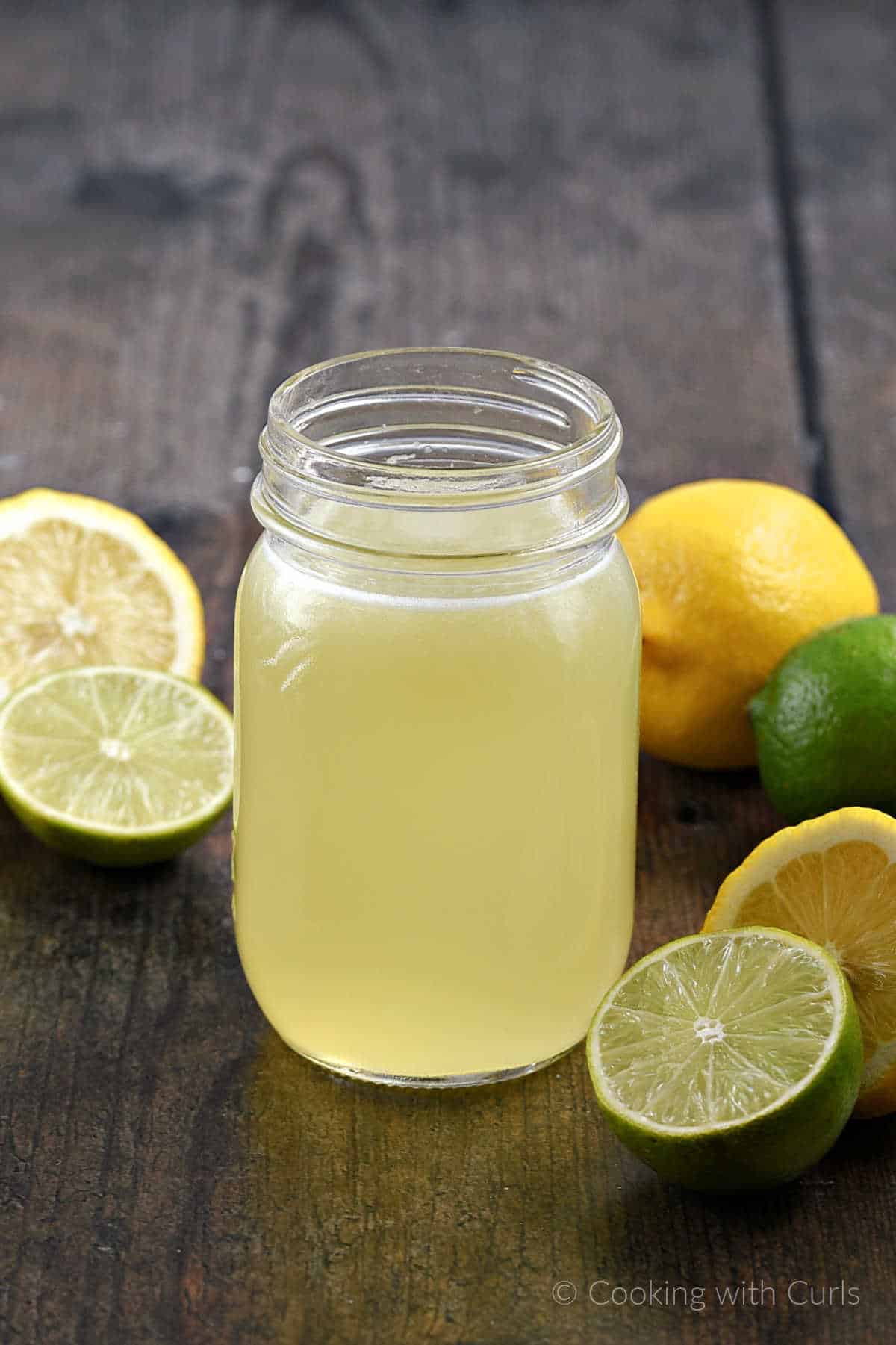 Sweet and sour mix in a glass jar surrounded by cut limes and lemons.