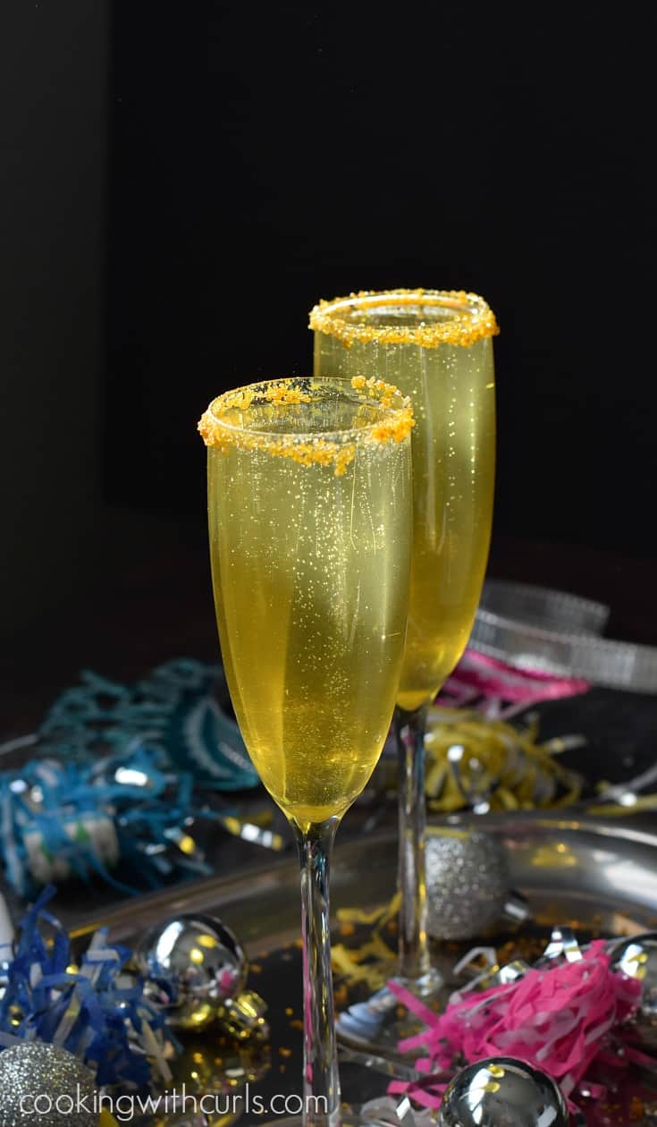 Two gold cocktails in gold sugar rimmed champagne flutes surrounded by new year's eve party decorations.