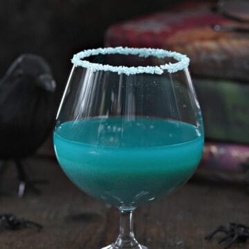 Teal blue Goblet of Fire cocktail recipe in a goblet glass in front of a stack of Harry Potter books.