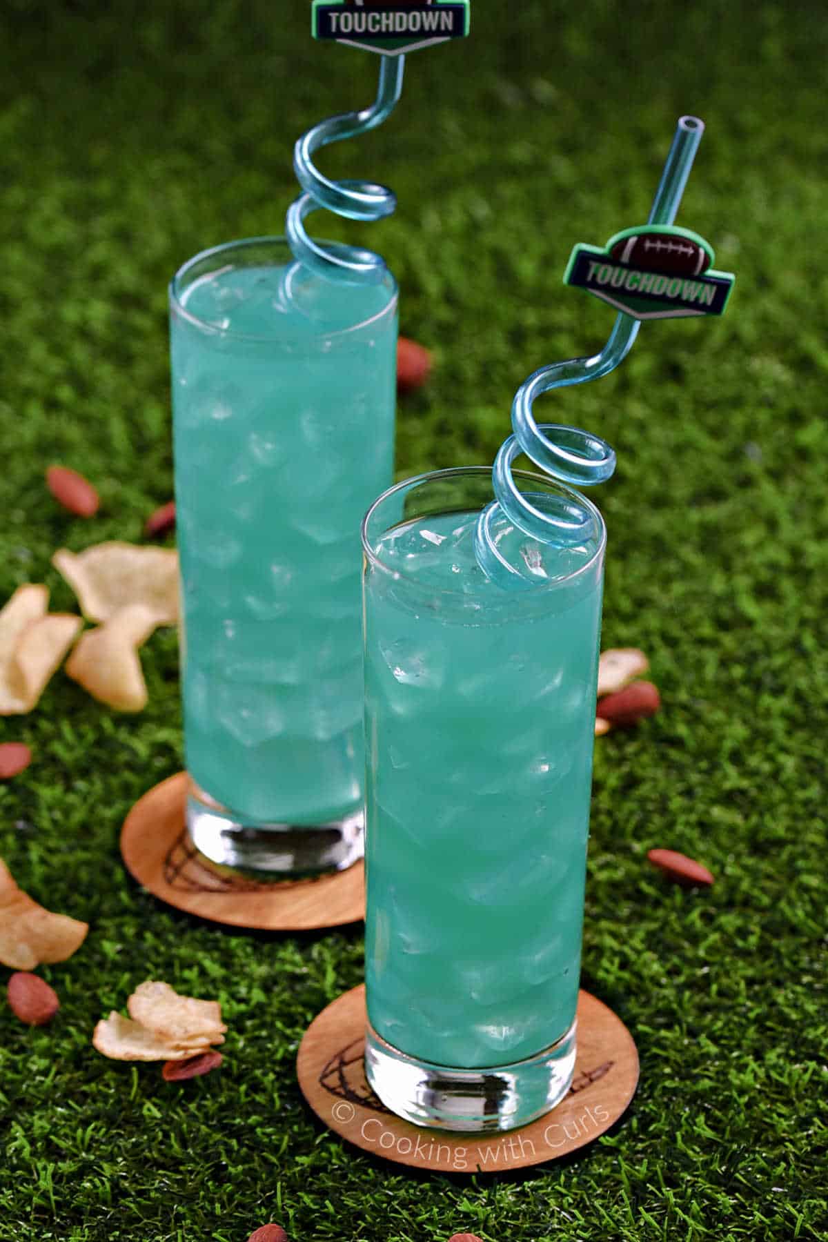 Two tall, skinny glasses filled with teal green drinks and a spiral straw.