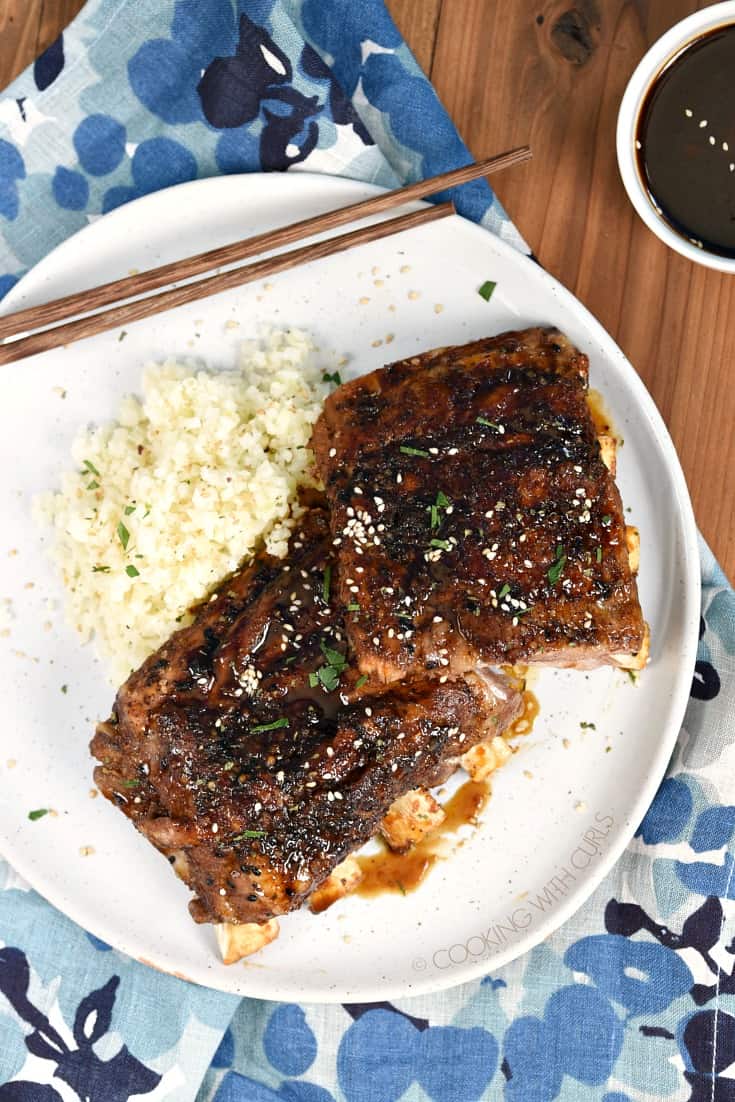 Looking down on Instant Pot Teriyaki Ribs on a white plate with cauliflower rice and a small bowl of teriyaki sauce in the upper right hand corner