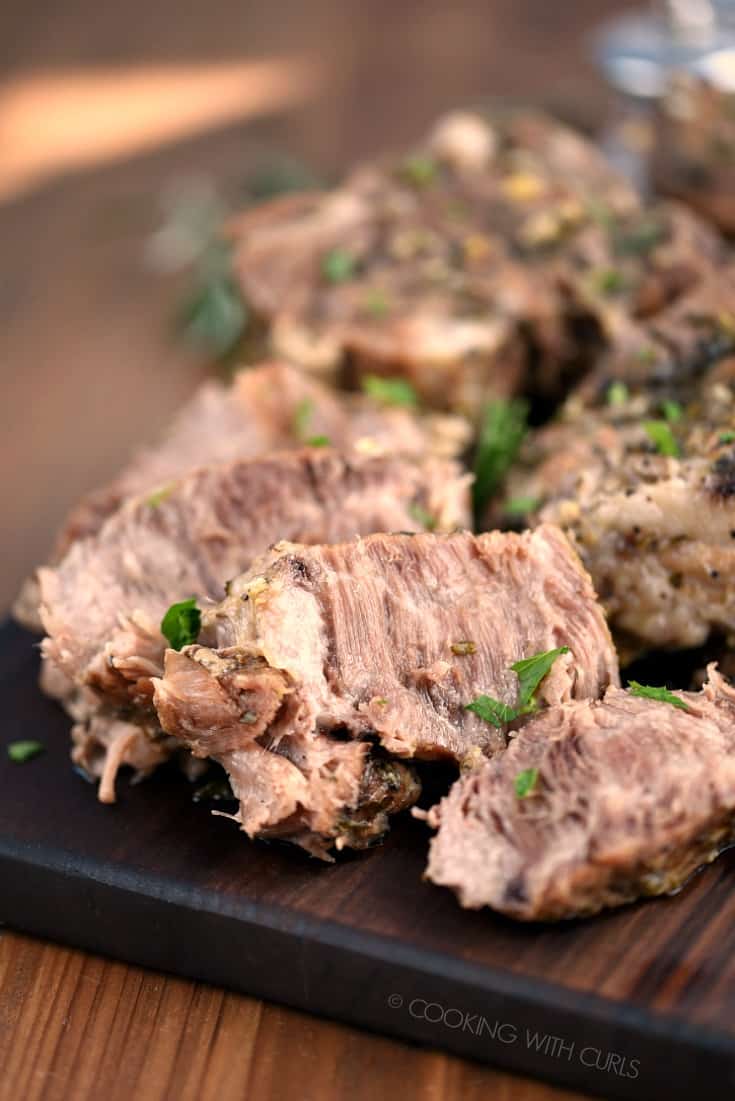 A close up image of sliced Instant Pot Rosemary Garlic Pork Roast on a wood cutting board.