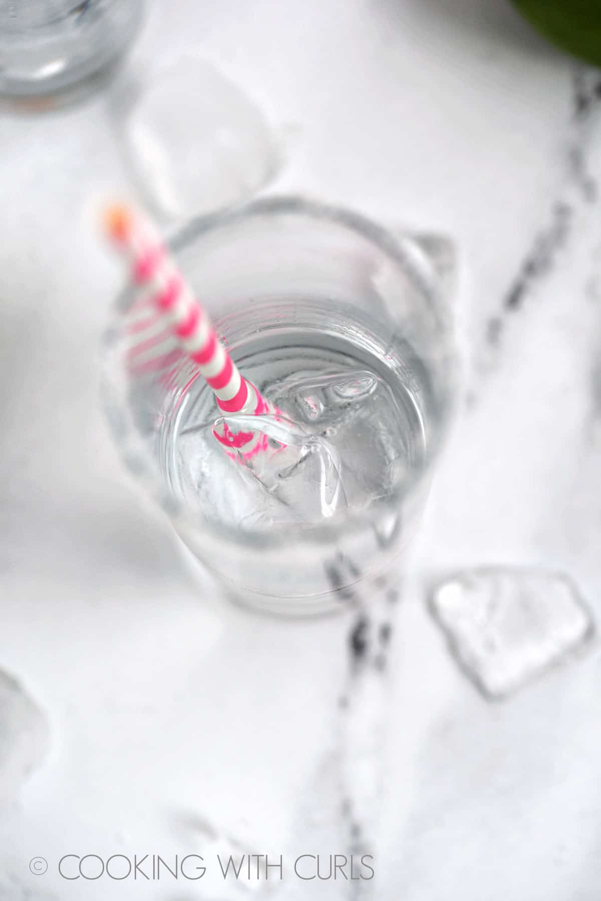 Tequila in a highball glass with ice cubes and pink and white striped straw. 