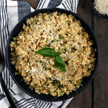 Looking down on a large bowl filled with basil risotto topped with grated Parmesan and fresh basil leaves.