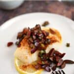 looking down on cherry salsa topped baked cod filet laying on two lemon slices on a white plate.