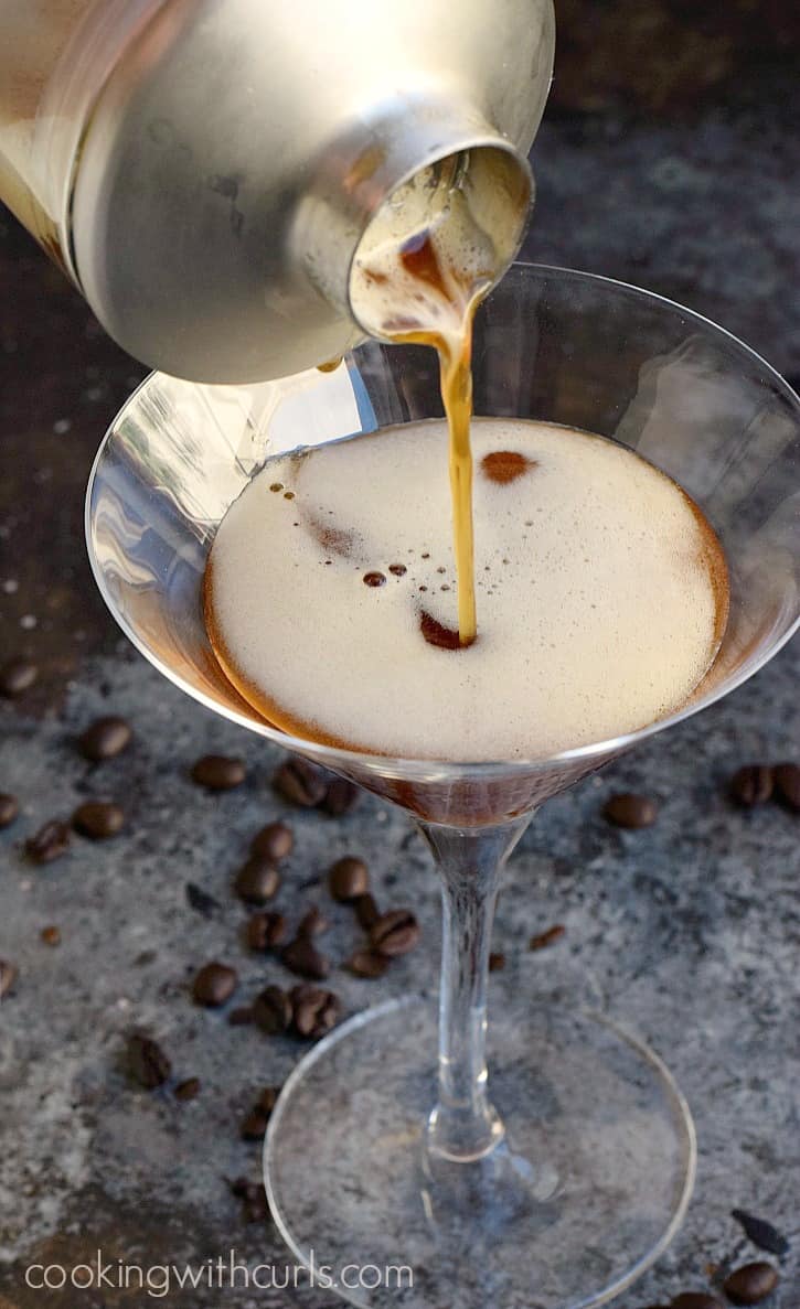 A silver cocktail shaker pouring an espresso martini into a martini glass.