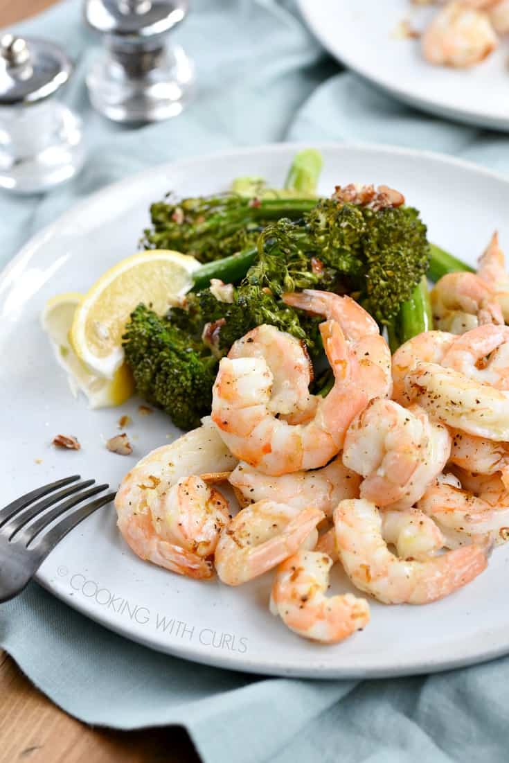 Shrimp, broccolini and lemon wedges on a large white plate