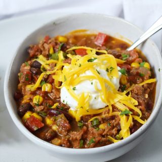 A bowl of Southwest Chili with Black Beans and Corn topped with sour cream and shredded cheddar cheese