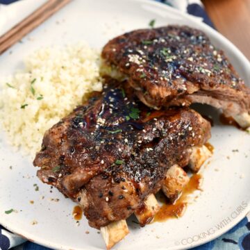 Two stacks of pork ribs on a plate next to cauliflower rice with a small bowl of teriyaki sauce in the corner