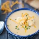 a dark blue bowl filled with potato cheese soup, and topped with croutons and shredded cheddar cheese with additional cheese in the background