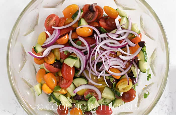 Thin slices of red onion on top of the tossed tomato cumber mixture. 