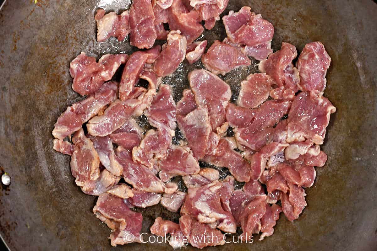 Thin strips of pork frying in oil in a wok. 