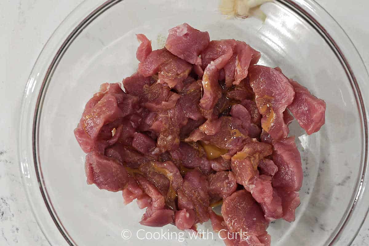 Thin strips of pork loin mixed with marinade in a large bowl. 