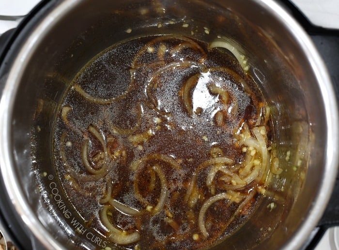Thinly sliced onions, garlic, soy sauce and chicken stock in the metal liner of a pressure cooker