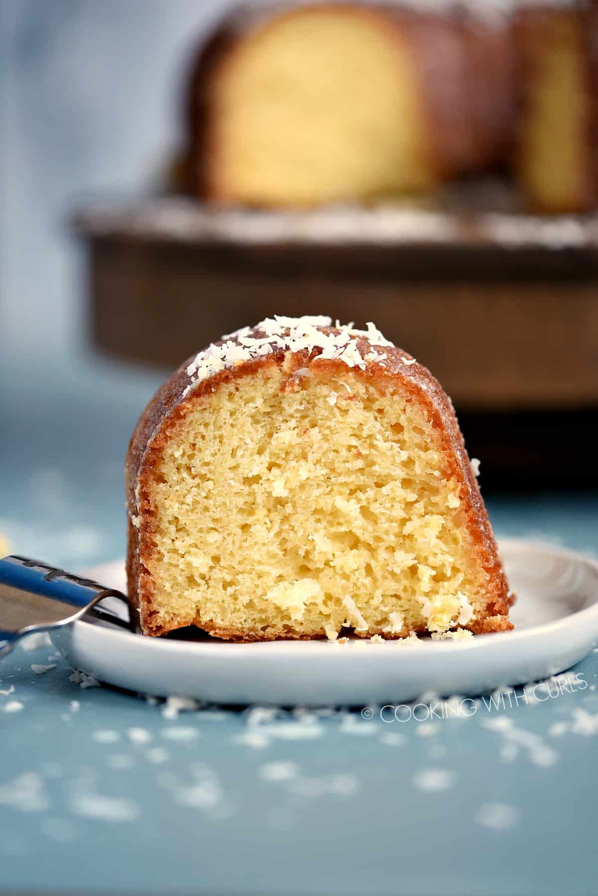 A slice of Bacardi Pina Colada Rum Cake on a small white plate with the remaining bundt cake in the background.