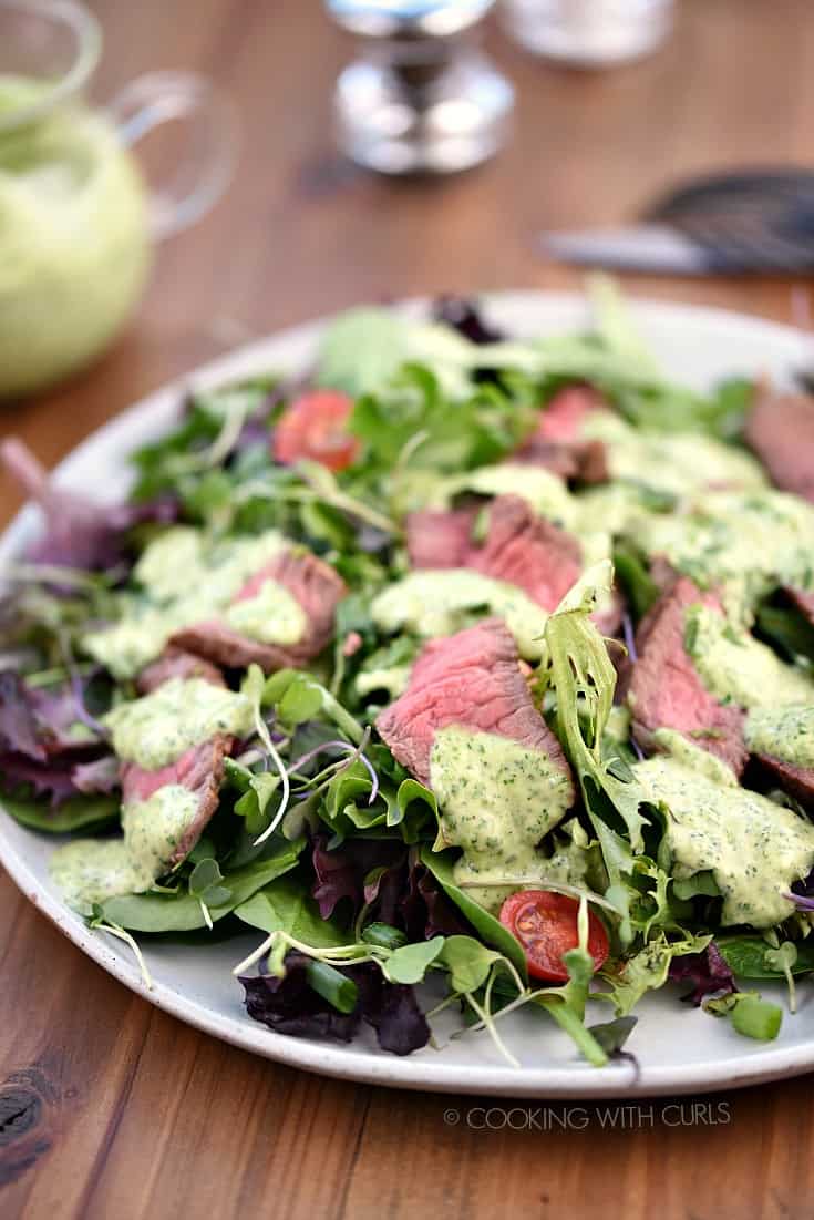 A large white plate topped with salad greens, sliced steak, cherry tomatoes and cilantro-lime dressing