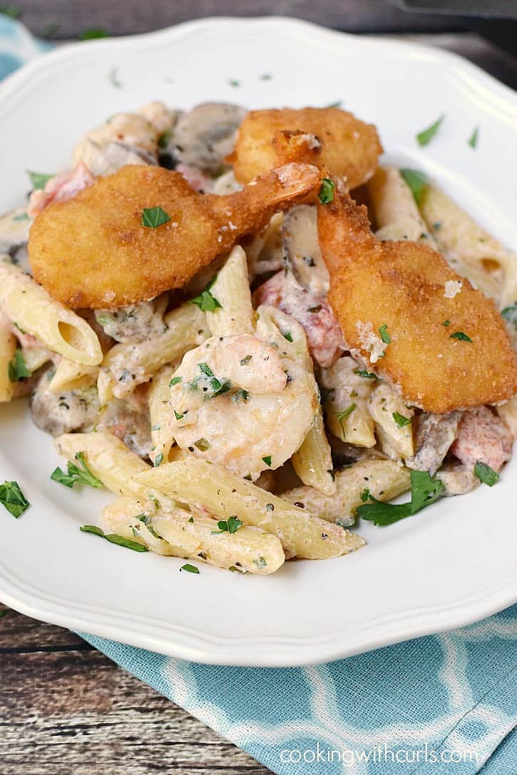 Creamy shrimp pasta topped with breaded shrimp and chopped parsley on a dinner plate.