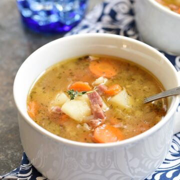 Two white bowls filled with Instant Pot Ham Bone and Potato Soup on a navy blue and white patterned napkin with a blue glass of water in the background