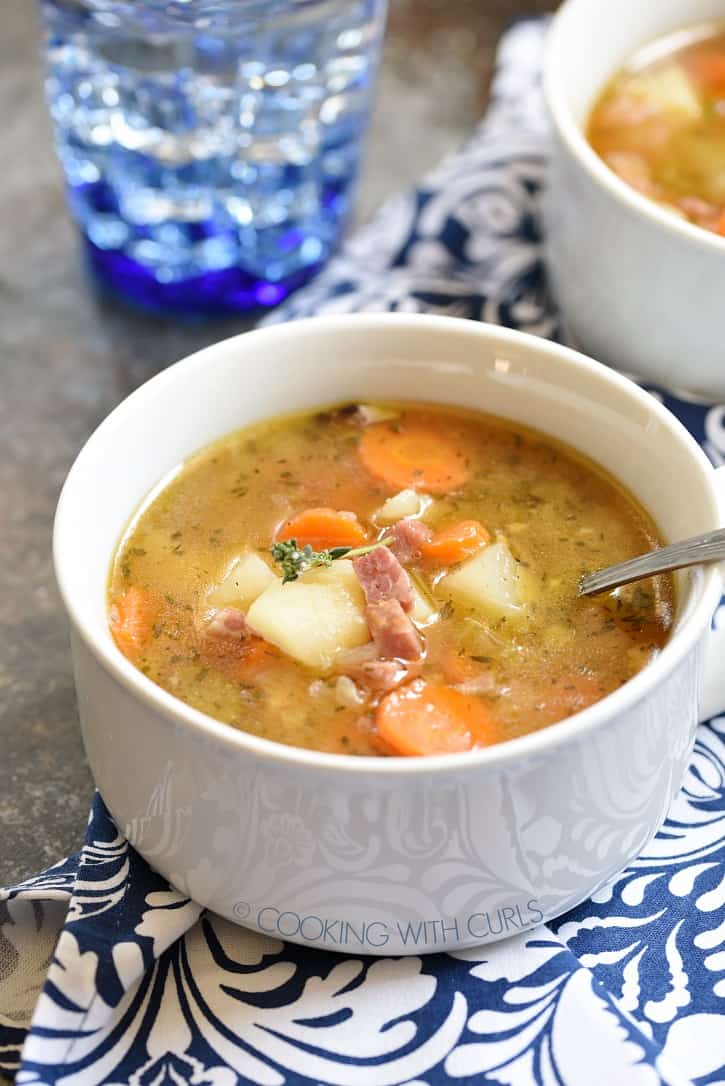 Two white bowls filled with Instant Pot Ham Bone and Potato Soup on a navy blue and white patterned napkin with a blue glass of water in the background