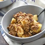 Instant Pot Apple Crisp in a white bowl with a black spoon leaning against the edge.