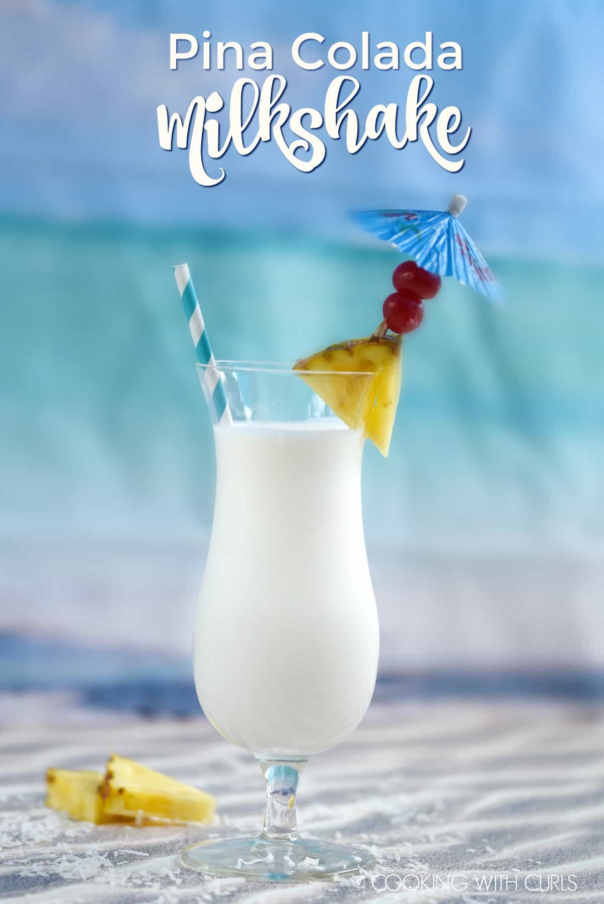 Creamy Pina Colada Milkshake in a hurricane glass that is garnished with a pineapple wedge, cherries and a blue paper umbrealla.