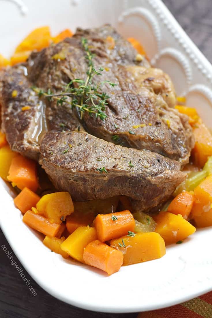 pot roast surrounded by carrots and squash in a white bowl.