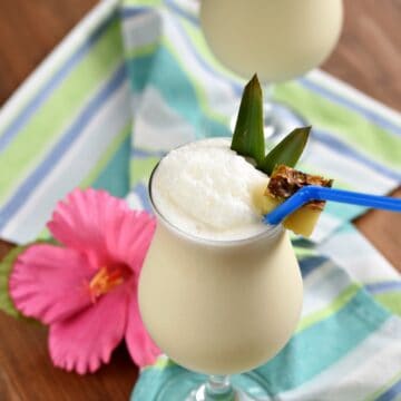 Looking down on two pina colada cocktails sitting on a striped napkin with straws and pineapple garnish