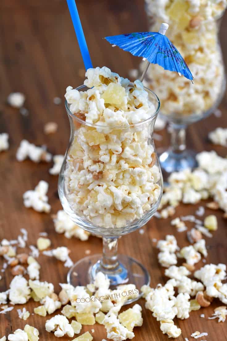 Pina Colada Popcorn overflowing a cocktail glass with a straw and paper umbrella sticking out the top of the glass