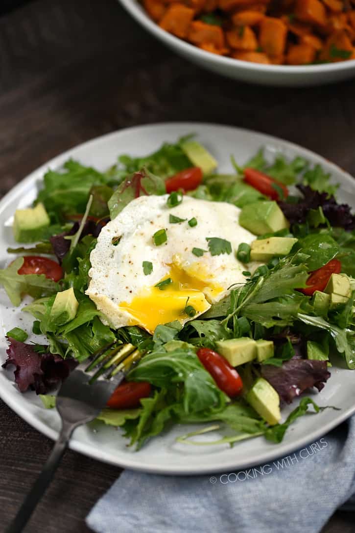 Poached egg with a broken yolk on salad greens with cherry tomatoes and diced avocado.