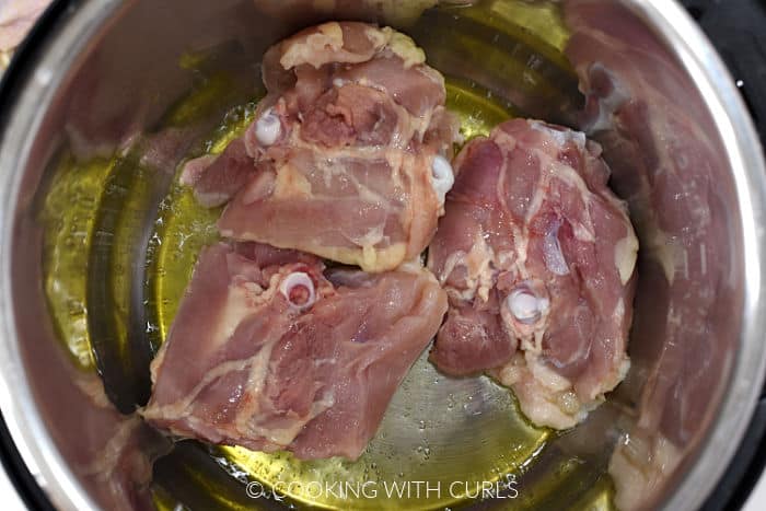 Three bone-in skin-on chicken thighs skin side down in hot oil. 