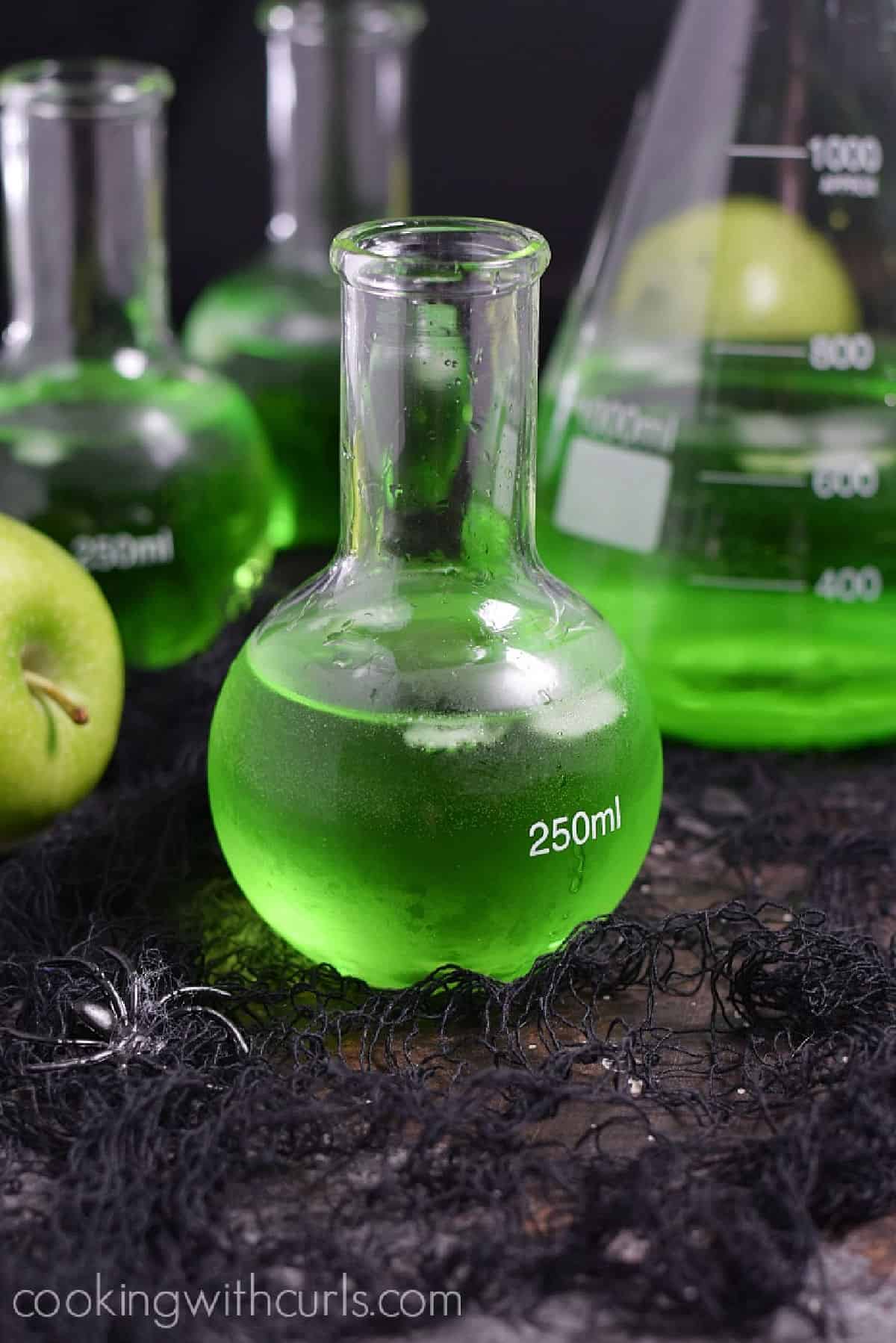 Three Poisoned Apple Cocktails in glass science bottles and a large beaker. 