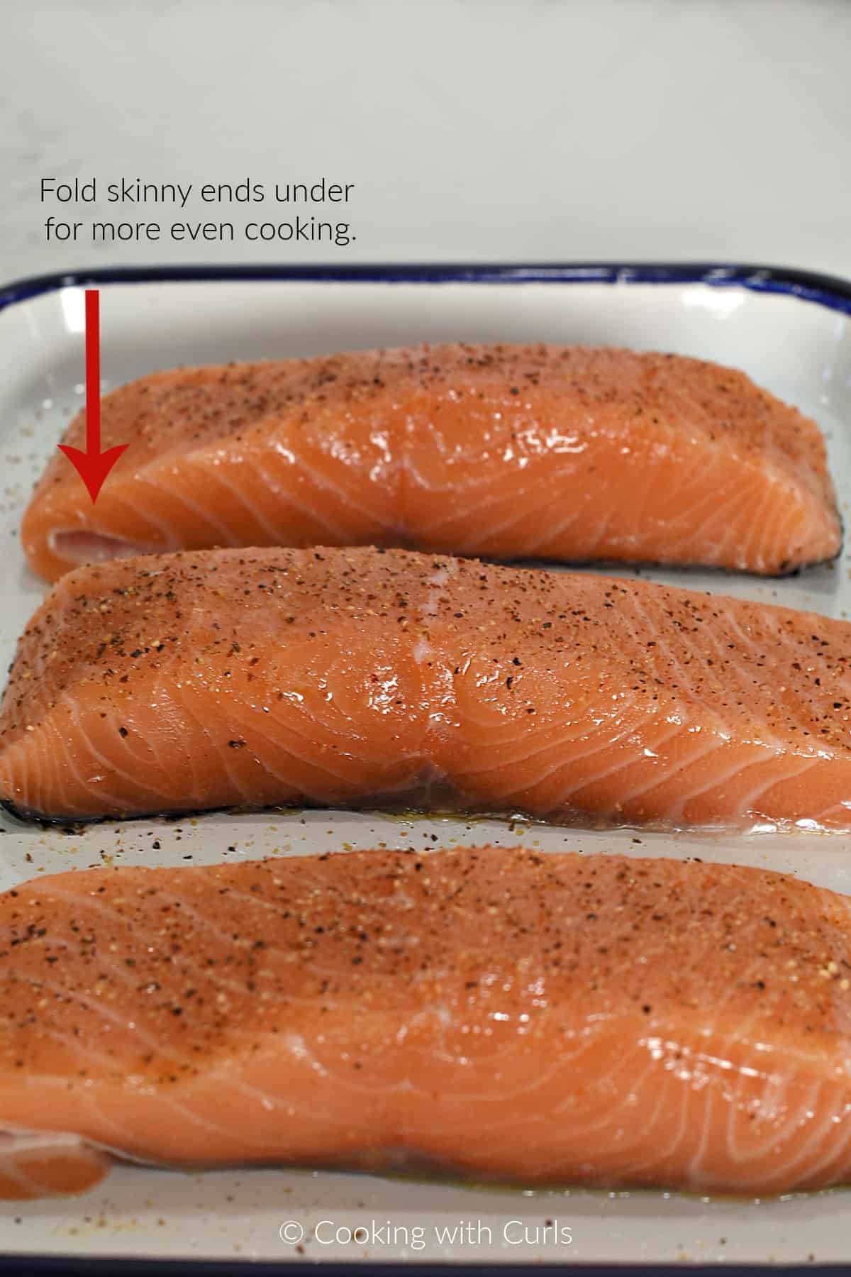 Three skin-on center-cut salmon filets on a platter sprinkled with garlic-pepper salt. 