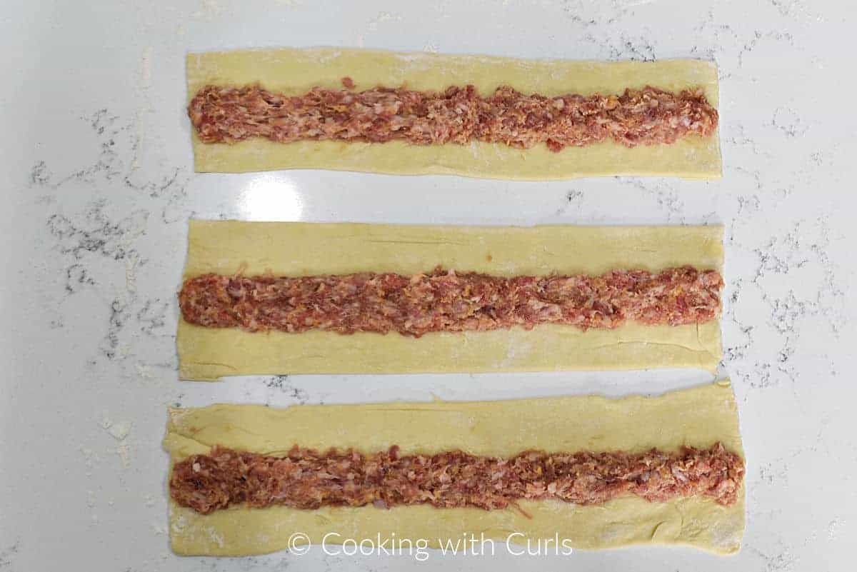 Three strips of puff pastry with sausage down the center. 