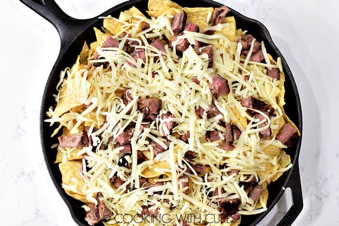 Tortilla chips, grated cheese and chunks of steak in a cast iron skillet. 