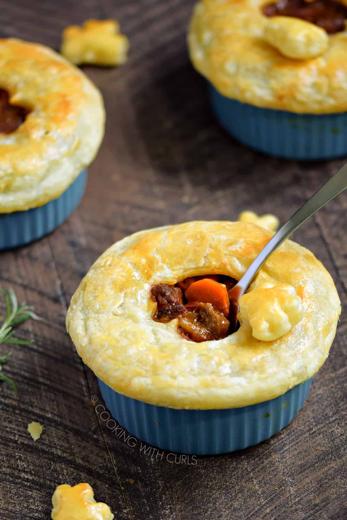 Puff pastry topped beef stew in a blue ramekin with two more in the background.