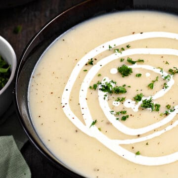 Traditional Irish Potato Leek Soup in a dark bowl drizzled with cream and sprinkled with minced parsley.