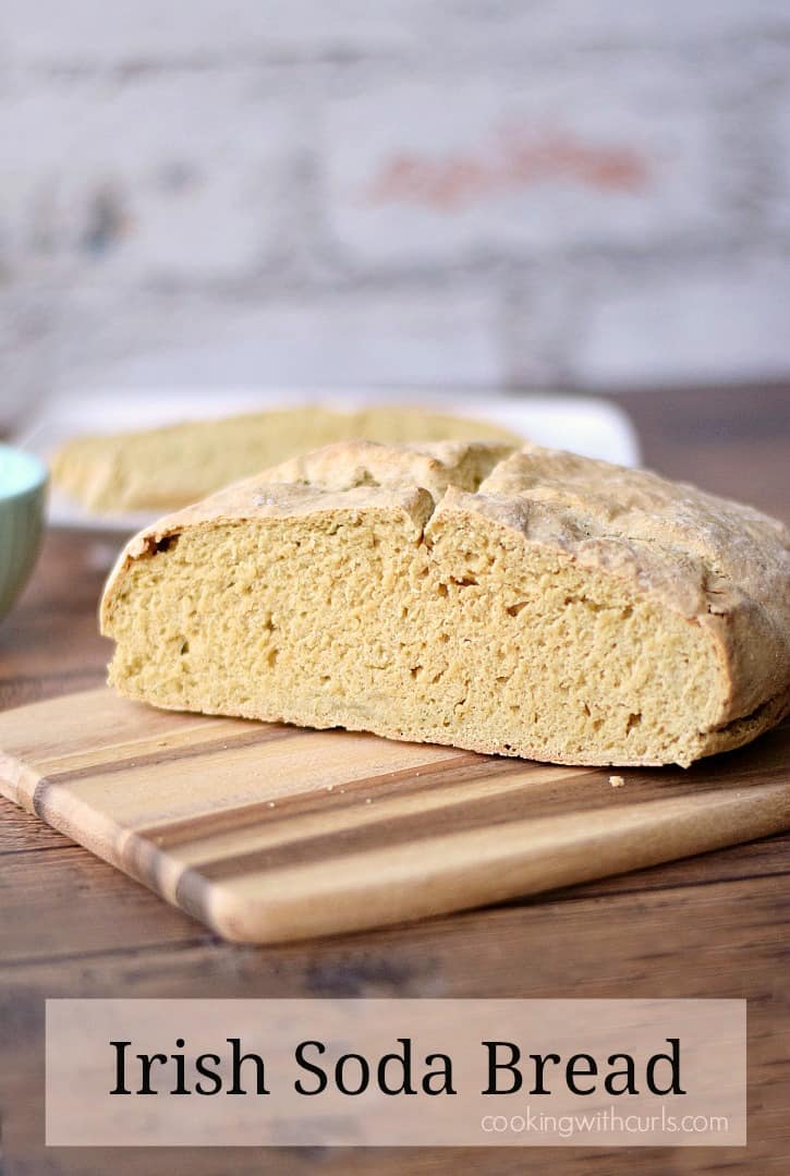 Irish soda bread on a wood cutting board with the end cut off and placed on a white plate in the background.