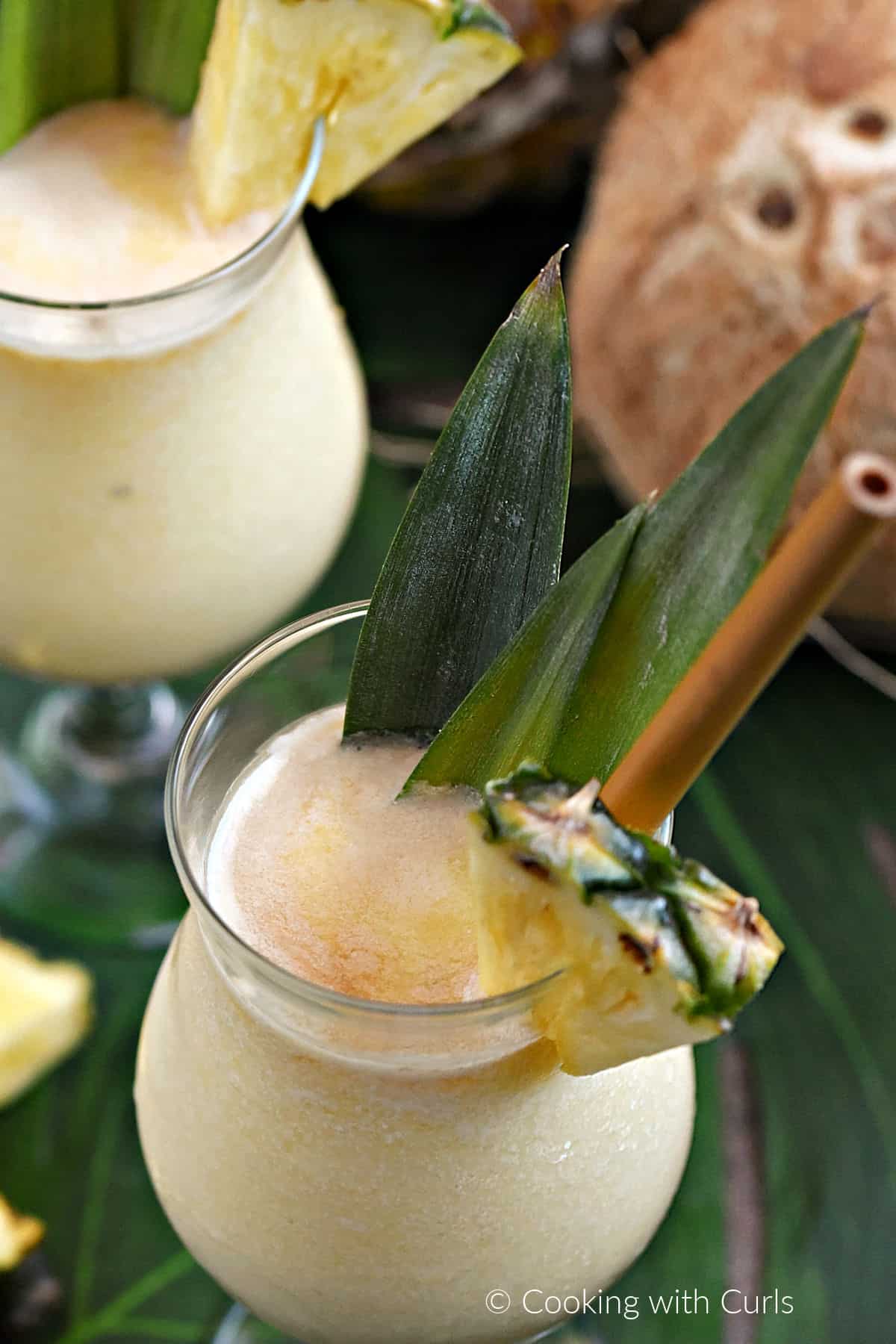 Looking down on two cocktail glasses filled with frozen Pina colada with dark rum floating on top and pineapple wedge and leaves as garnish.