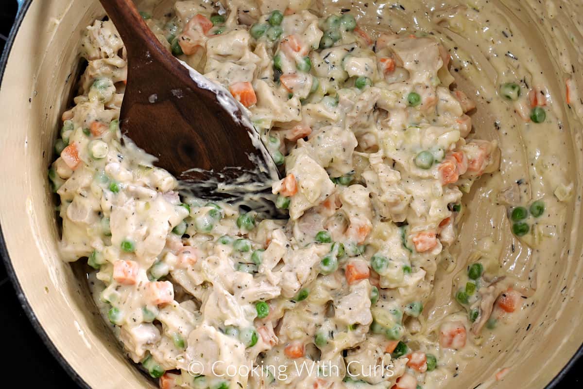 Turkey and cream sauce mixed with a wooden spoon in a Dutch oven. 