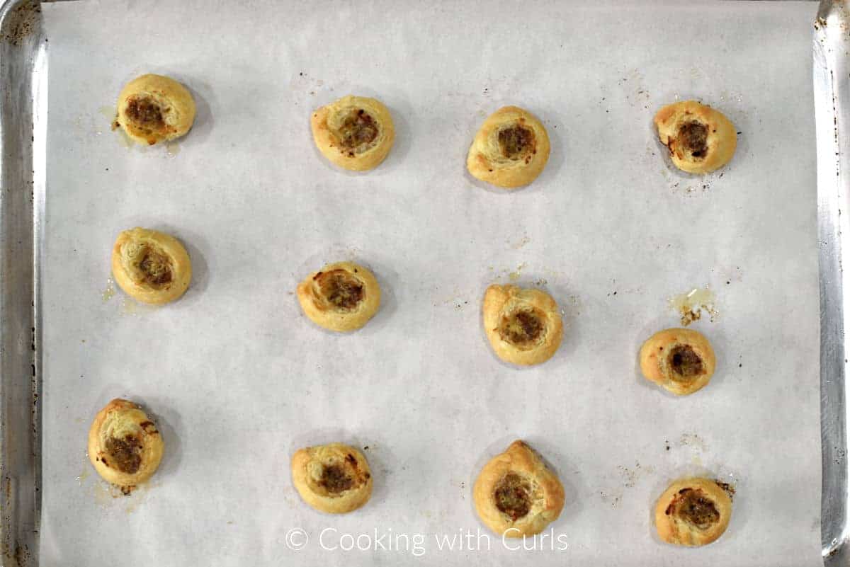 Twelve baked puff pastry sausage bites on a parchment lined baking sheet. 