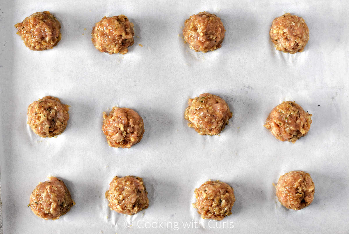 Twelve teriyaki chicken meatballs on a parchment lined sheet pan.