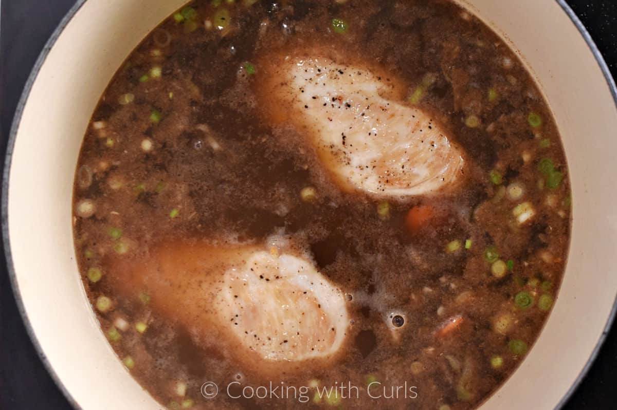 Two boneless chicken breasts in the pot with chicken stock and aromatics. 