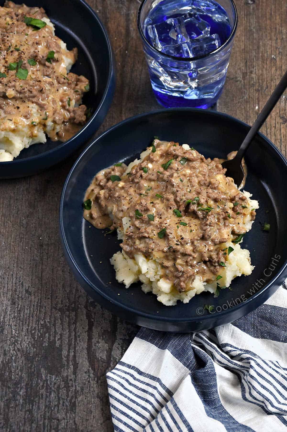 Two-bowls-of-Hamburger-Gravy-poured-over-mashed-potatoes-with-chopped-parsley-garnish.