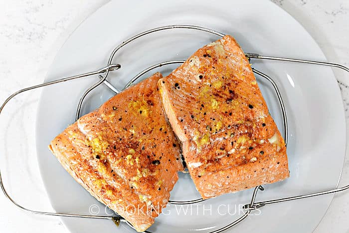 Two cooked salmon filets on a wire trivet sitting  on a white plate. 