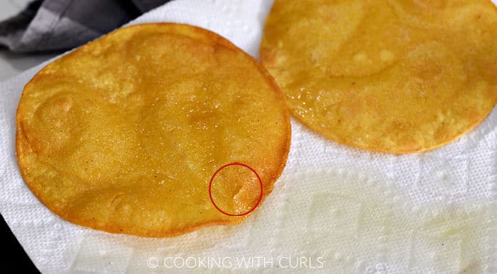 Two fried corn tortillas draining on a paper towel. 