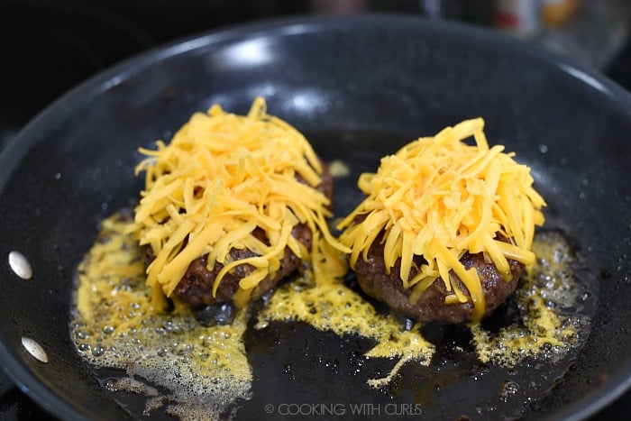 Two half-pound burgers topped with shredded, cheddar cheese in a skillet. 